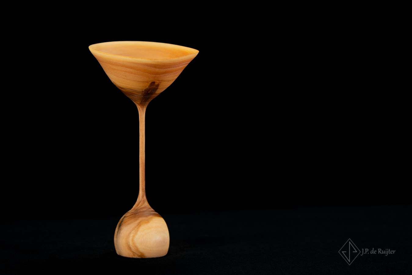 Een ornament van hout, elegant dun in de vorm van een bloem, waarvan de kelk lijkt op een coctail glas.