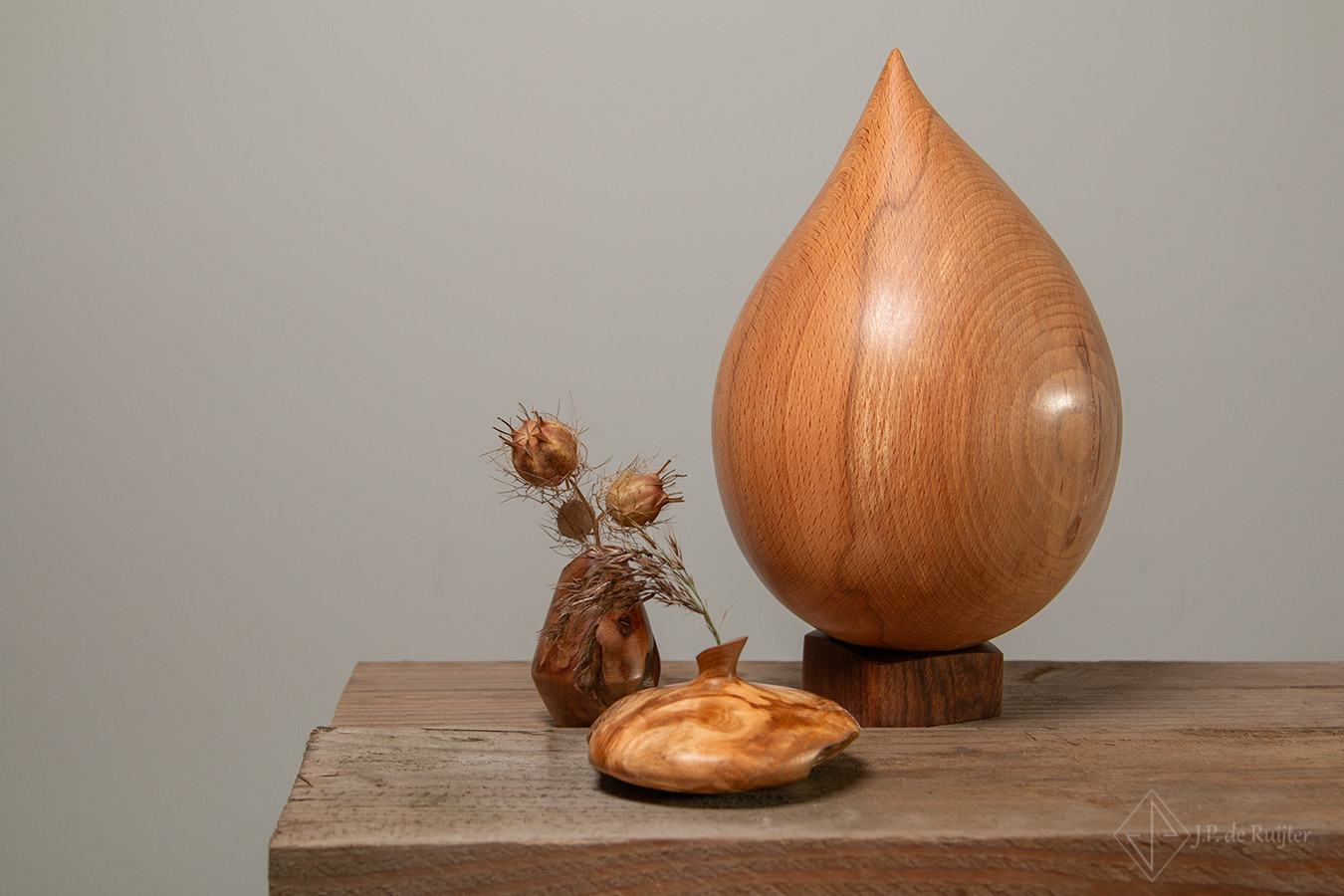 Urn van beuken hout in ddruppel vorm. Daarnaast twee miniatuur vaasjes voor een klein droog bloempje.