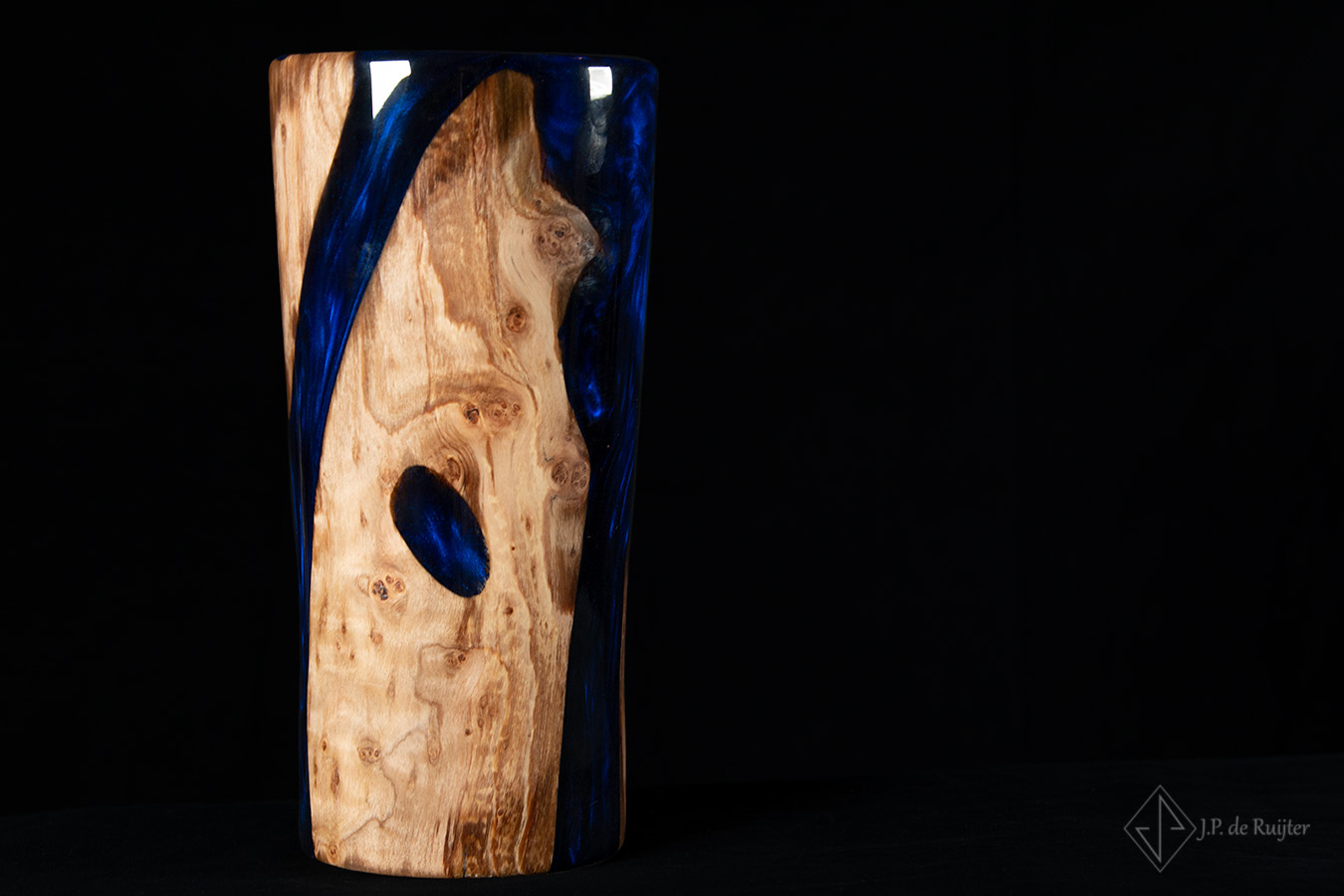 Vaas in strakke hoge vorm van schijnbeuken hout met strakke lijnen er in, gevuld met epoxy in blauw. Uniek, exclusief en handgemaakt.  Vooraanzicht.